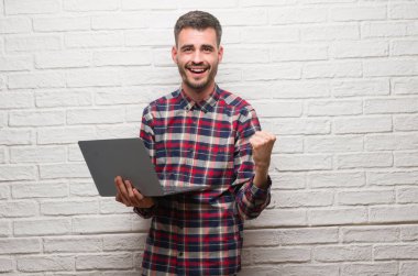 Duygu tezahürat genç yetişkin adam gurur çığlık ve zafer ve başarı çok heyecanlı, kutluyor dizüstü kullanarak tuğla duvar üzerine