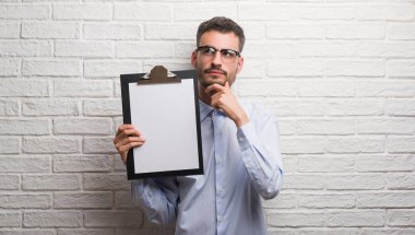 Genç Yetişkin iş adamı Pano ciddi bir yüz düşünme hakkında soru, çok karışık fikir tutan tuğla duvarın üzerinden