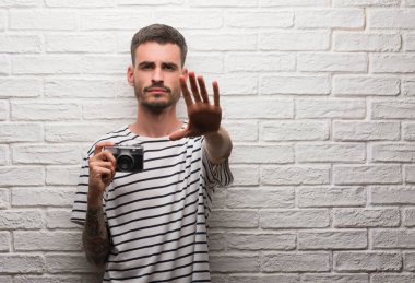 Vintage fotoğraf makinesi beyaz tuğla duvarın üzerinden açık eliyle dur işareti ile ciddi ve kendine güvenen ifade, savunma jest yapıyor ayakta tutan genç adam