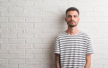 Genç yetişkin adam akıllı yüzünde ciddi düşünme emin bir ifade ile beyaz tuğla duvarın üzerinden ayakta