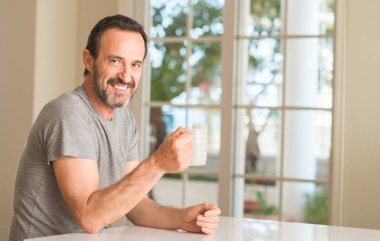 Orta yaş adam ayakta ve diş gösterilen kendine güvenen bir gülümsemeyle gülümseyerek mutlu bir yüz ile bir fincan kahve içme