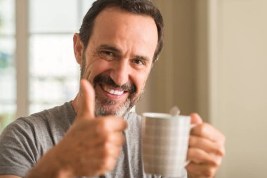 Ok işareti, başparmak ile parmak, mükemmel işareti yapıyor kocaman bir gülümseme ile mutlu bir fincan kahve içme orta yaş erkek