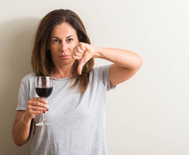 Kızgın yüz, eksi işareti aşağı antipati başparmak ile gösterilen, ret kavramı ile bir bardak kırmızı şarap içme orta yaş kadın