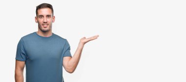 Casual yakışıklı genç gülümseyen neşeli sunulması ve kameraya bakarak avucunun ile işaret.