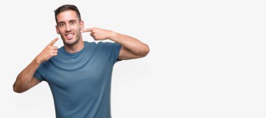 Kendinden emin gösterilen ve işaret parmakları diş ve ağız ile gülümseyen yakışıklı genç casual adam. Sağlık kavramı.