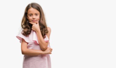 Emin çapraz kollar ve çeneme kaldırdı el ile gülümseme ile kameraya bakarak pembe elbise esmer Latin kız. Pozitif düşünce.