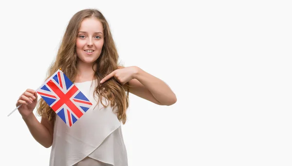 年轻的金发女人拿着英国国旗惊讶的脸指着自己的手指 — 图库照片