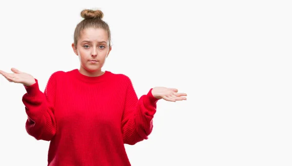 腕と手を上げてのお団子と赤のセーター無知と混乱して式を身に着けている若いブロンドの女性 疑いのコンセプト — ストック写真