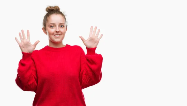 年轻的金发女人穿着包子和红色毛衣显示和指向十的手指 而微笑着自信和快乐 — 图库照片
