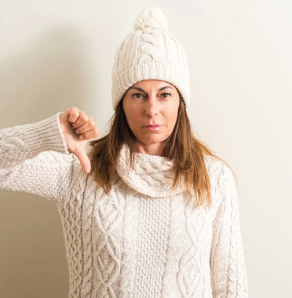 Middle age woman wearing wool winter cap with angry face, negative sign showing dislike with thumbs down, rejection concept