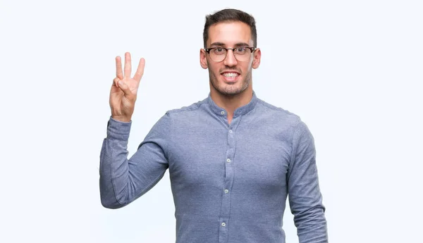 英俊的年轻优雅的男子戴眼镜显示和指着手指数三 而微笑着自信和快乐 — 图库照片