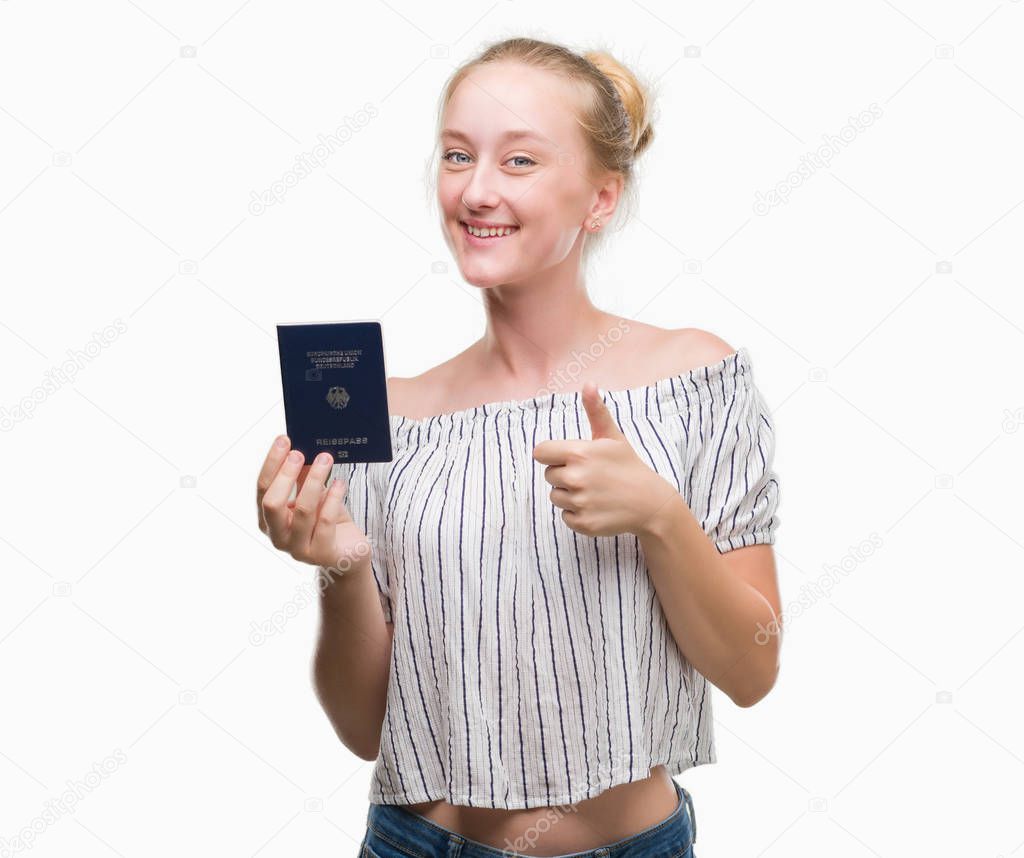 Blonde teenager woman holding passport of Germany happy with big smile doing ok sign, thumb up with fingers, excellent sign