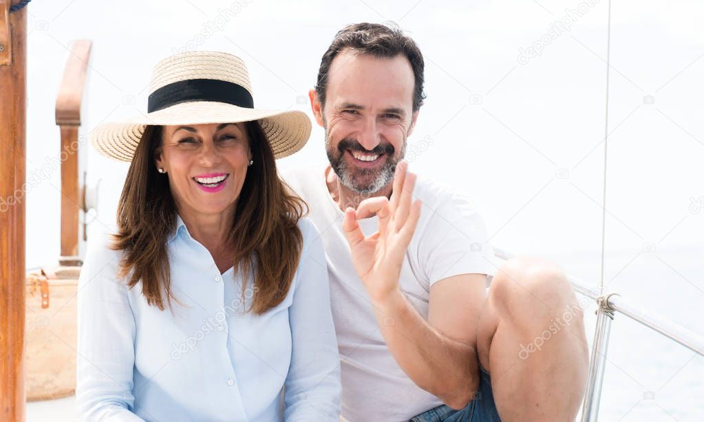 Middle age couple traveling on sailboat doing ok sign with fingers, excellent symbol