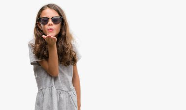 Esmer Latin kız bir öpücük el ile güzel ve seksi olmak hava üfleme kamera bakarak güneş gözlüğü takıyor. Aşk ifade.
