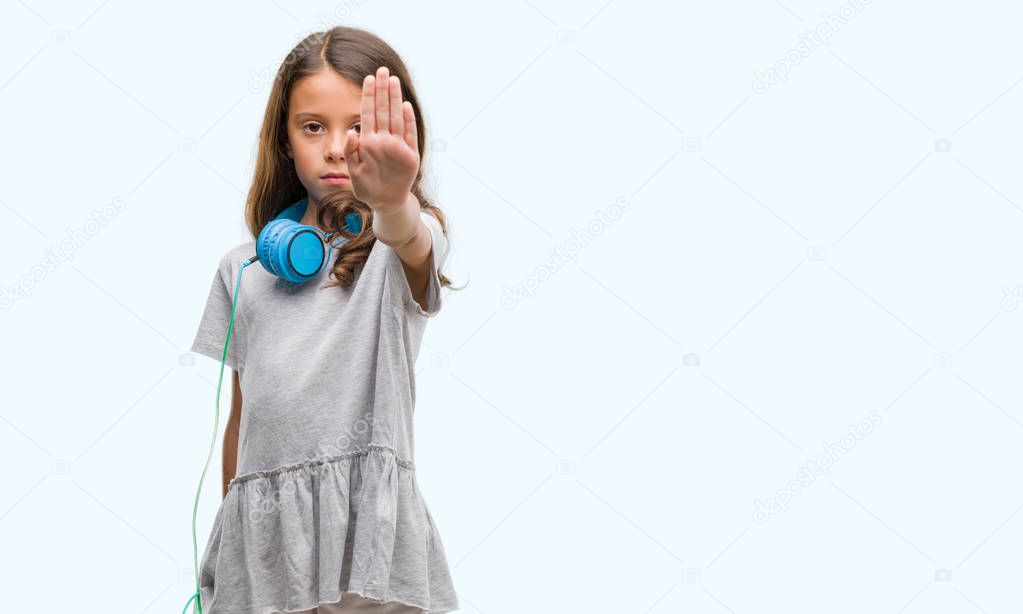 Brunette hispanic girl wearing headphones with open hand doing stop sign with serious and confident expression, defense gesture