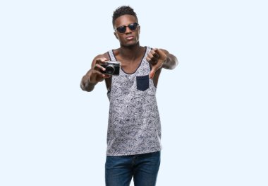 Başparmak aşağı, ret kavramı ile eksi işareti gösteren genç Afro-Amerikan adam kızgın yüz tutan vintage kamerayla, sevmemek