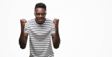 Gözlük ve Donanma kutluyor t-shirt giyen genç Afro-Amerikan adam şaşırttı ve başarı için kaldırdı kollarını açarak hayret ve gözleri açık. Kazanan kavramı.