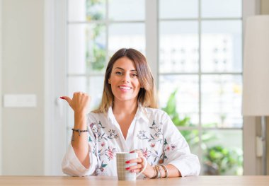 Genç kadın evde kahve el ve parmak ile mutlu yüz gülümseyen ile yukarı dönük içme