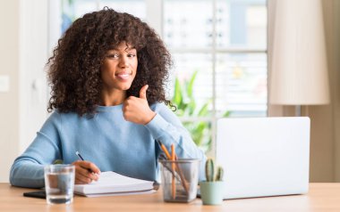 Afrikalı-Amerikalı kadın evde eğitim yapıyor ok işareti, kocaman bir gülümseme ile mutlu bir bilgisayar dizüstü kullanarak başparmak yukarı parmaklarıyla, mükemmel işareti