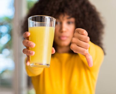 Afrikalı-Amerikalı kadın evde kızgın yüzü, eksi işareti aşağı antipati başparmak ile gösterilen, ret kavramı ile sağlıklı meyve suyu içme