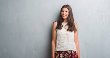 Grunge gri duvar ayakta ve diş gösterilen kendine güvenen bir gülümsemeyle gülümseyerek mutlu bir yüz ile genç esmer kadın