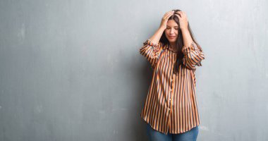 Genç esmer kadın grunge gri duvar çünkü umutsuz ve stresli baş ağrısı acı yüzünden acı ve migren. Ellerini kafasına.