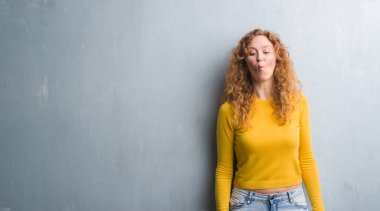 Genç Kızıl saçlı kadın gri grunge duvar yapım balık yüzüne dudaklı, çılgın ve komik bir jest. Komik ifade.