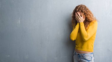 Gri grunge duvar yüz eller ile ağlayarak süre kapsayan üzgün ifade ile genç Kızıl saçlı kadın. Depresyon kavramı.