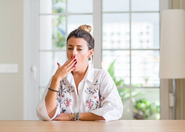 Молодая женщина дома скучала зевая усталый закрывающий рот рукой. Беспокойство и сонливость
.