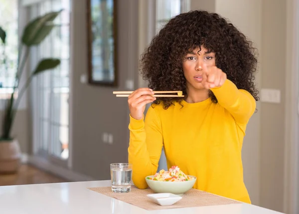 African american woman eating asian rice at home pointing with finger to the camera and to you, hand sign, positive and confident gesture from the front