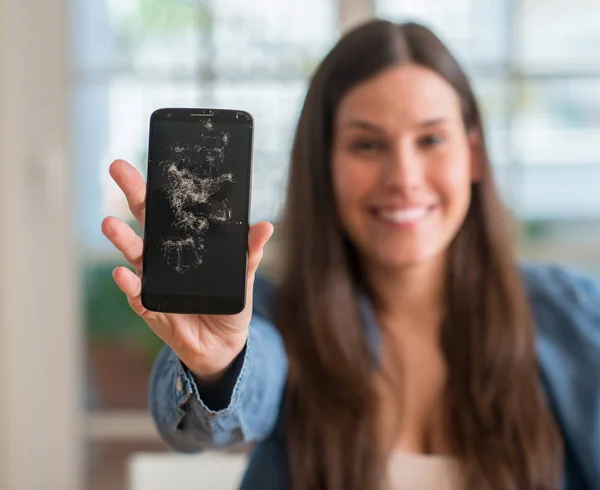 Brunette young woman holding broken smartphone with a happy face standing and smiling with a confident smile showing teeth