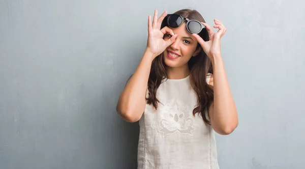 Молодая Брюнетка Женщина Над Гранж Серый Стены Модных Солнцезащитных Очках — стоковое фото