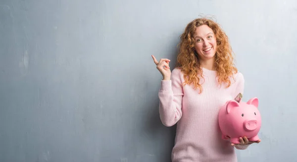 Young Redhead Woman Grey Grunge Wall Holding Piggy Bank Dollar — Stock Photo, Image
