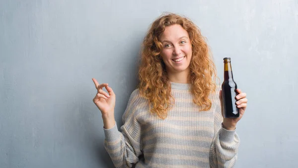 Joven Pelirroja Sobre Pared Grunge Gris Sosteniendo Botella Cerveza Muy — Foto de Stock