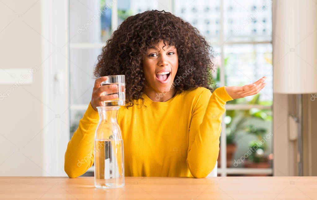 African american woman drinking a glass of water at home very happy and excited, winner expression celebrating victory screaming with big smile and raised hands