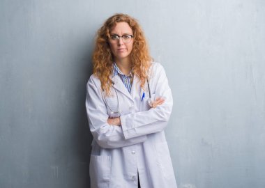 Gri grunge duvar yüz çapraz kolları olan bir ceket şüpheci ve sinir, onaylamayan ifade giyen genç redhead doktor kadın. Negatif kişi.