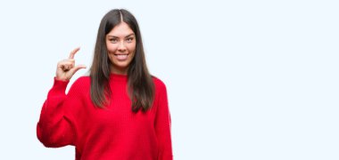 Genç güzel İspanyol giyen kırmızı kazaklı gülümseyen ve boyutu işi el ile kendinden emin eller parmakları ile seyir ve fotoğraf makinesi oturum açın. Ölçü kavramı.