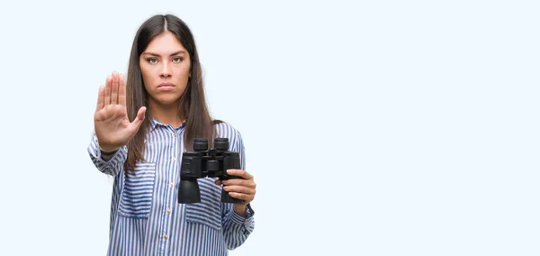 年轻的西班牙裔妇女手持双筒望远镜张开手做停止标志认真和自信的表达 防御姿态 — 图库照片