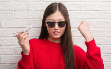 Genç Çinli kadın tutmak uçak oyuncak tuğla duvarın üzerinden rahatsız ve boşa çıkarmak ile öfke, çılgın da yükseltilmiş el ile bağırmaya kavramı öfke