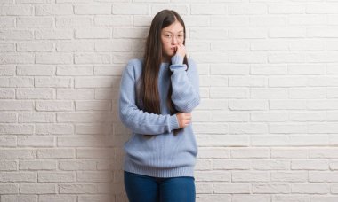 Tırnak ısırma dudaklarından eller genç Chinise kadın stresli ve gergin ile beyaz tuğla duvarın üzerinden. Anksiyete sorunu.