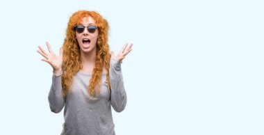 Güneş gözlüğü çok mutlu ve heyecanlı giyen genç Kızıl saçlı kadın, kocaman bir gülümseme ile çığlık zaferini kutluyor ve ellerini kaldırdı kazanan ifade