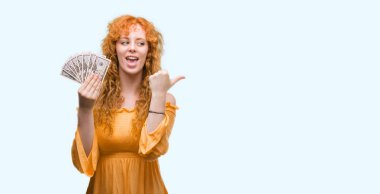 İşaret ve başparmak kadar mutlu yüz gülümseyen tarafı ile gösterilen dolar tutan genç Kızıl saçlı kadın