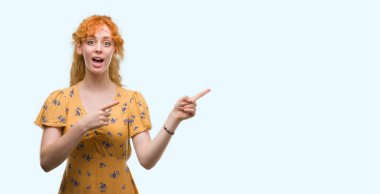 Hayret ve el ile sunulması ve parmak ile işaret ederken kameraya gülümseyen genç Kızıl saçlı kadın.