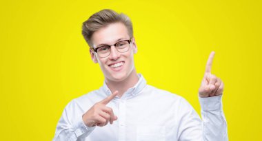 Gülümseyen ve iki elleri ve parmakları ile tarafına işaret kamera bakarak genç yakışıklı sarışın adam.