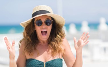 Orta yaş esmer kadın büyük gülümseme ile çığlık zaferini kutluyor ve ellerini kaldırdı havuzu çok mutlu ve heyecanlı, kazanan ifade tarafından güneş gözlüğü takıyor