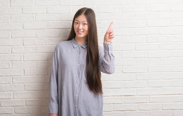 幸せそうな顔でのアイデアや質問ポインティング指と驚かれるレンガ壁を越えて若い中国女性がナンバーワンします — ストック写真