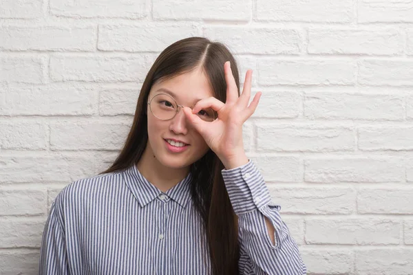 指の間から見て目に手で サインをして笑っている幸せそうな顔でレンガの壁以上の若い中国ビジネス女性 — ストック写真