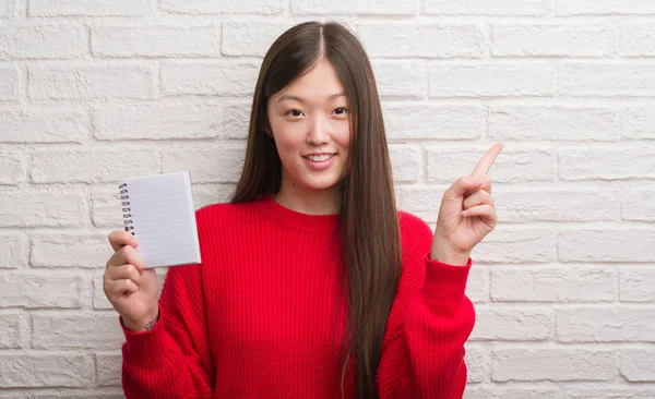 Joven Mujer China Sobre Pared Ladrillo Mostrando Cuaderno Blanco Muy —  Fotos de Stock