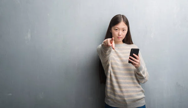 Молода Китайська Жінка Над Сірий Стіни Дивлячись Смартфон Вказуючи Пальцем — стокове фото