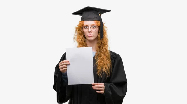 年轻的红发女子身穿毕业制服持有学位 自信地表达了对聪明面孔的认真思考 — 图库照片